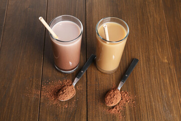 Delicious protein shakes in glasses and spoons with powder on wooden table