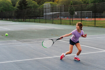 Smiling child swings tennis racket at incoming ball