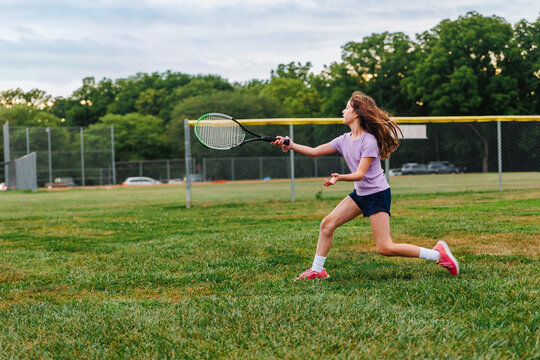 A running athletic girl swings a tennis racket in field