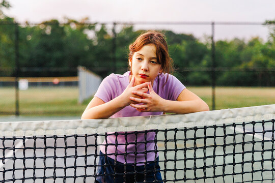 Portrait of thoughtful girl leaning on net at tennis court