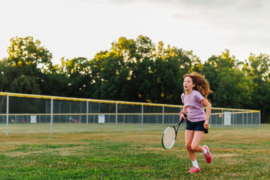 A girl runs through field with tennis racket
