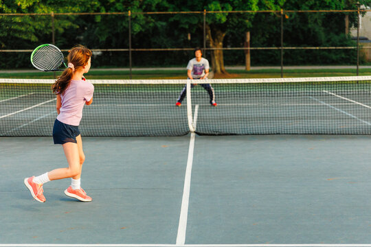 A girl and father play tennis together in summer