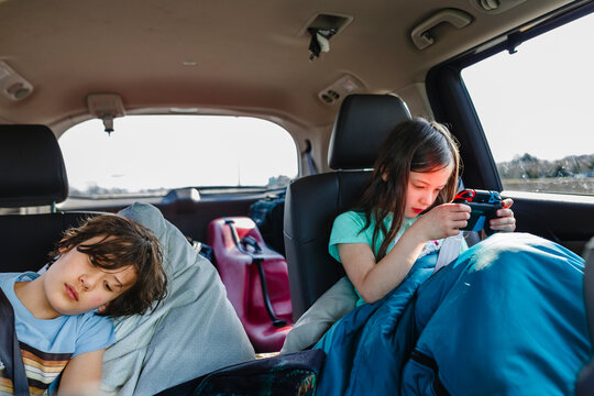 Two children sit in a car loaded for road trip playing video games
