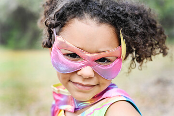 Close-up of a young girl in a superhero mask smiling, with curly