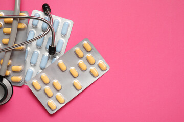 Different antibiotic pills in blisters and stethoscope on pink background, flat lay. Space for text
