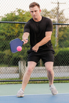 Young man concentrating on hitting a pink pickleball.