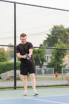 Young man smiling and hitting a pink pickleball on court.