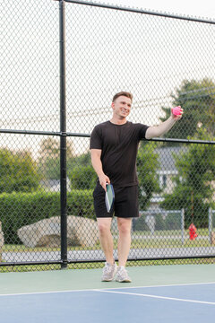 Young man smiling and holding a pink pickleball and paddle.