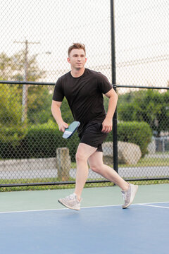 Young man in action playing pickleball on an outdoor court.