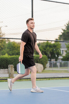 Young man walking on pickleball court holding a paddle.