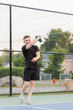 Young man smiling and swinging paddle on pickleball court.