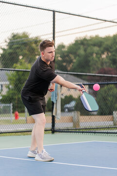 Young man hitting a pink pickleball with a paddle on court.