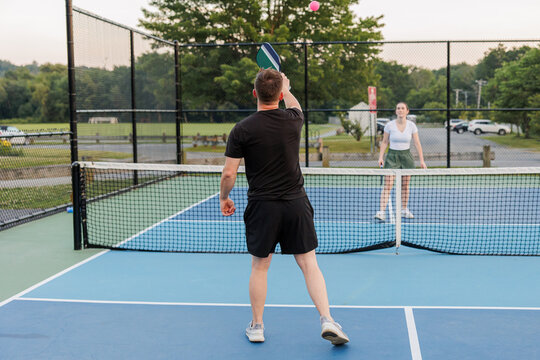 Man and woman playing pickleball, man preparing to hit the ball.