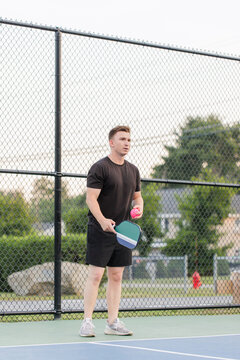 Young man preparing to serve with a pink pickleball on court.