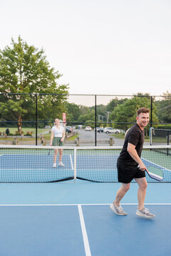 Woman and man playing pickleball on court smiling, enjoying the game