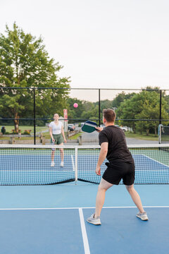 Man and woman engaged in a pickleball match on a blue outdoor court.