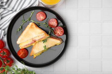 Pieces of toasted bread with melted cheese, ham and tomatoes on white tiled table, top view. Space for text