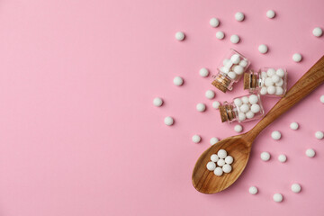 Homeopathic remedy. Glass bottles, pills and wooden spoon on pink background, flat lay. Space for text