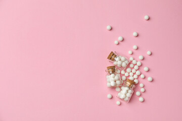 Homeopathic remedy. Glass bottles and pills on pink background, flat lay. Space for text