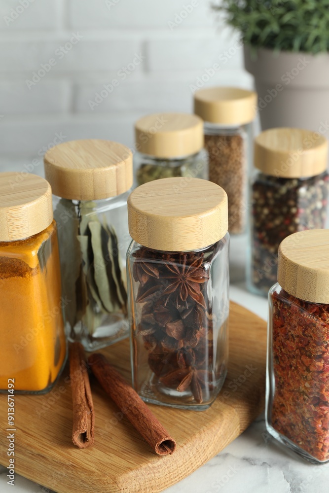 Wall mural Different spices in glass jars on white marble table