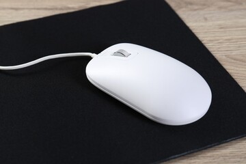 White computer mouse and black mousepad on wooden table, closeup