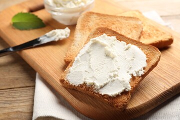 Delicious toasted bread slices with cream cheese on wooden table, closeup