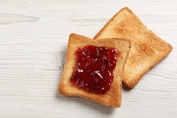 Delicious toasted bread slices with jam on white wooden table, top view