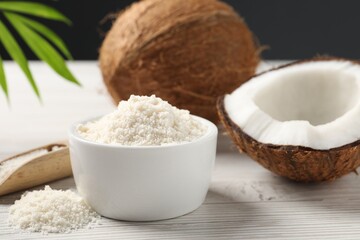 Fresh coconut flour in bowl, nuts, scoop and palm leaf on white wooden table