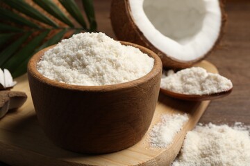 Coconut flour in bowl, spoon and fresh fruit on wooden table, closeup