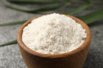 Organic coconut flour in bowl on grey table, closeup