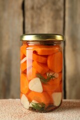 Tasty pickled vegetables in jar on beige textured table, closeup