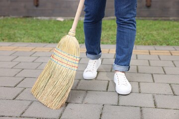 Woman with corn straw broom sweeping pavement outdoors, closeup