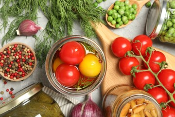 Different pickled products in jars and fresh ingredients on grey table, flat lay