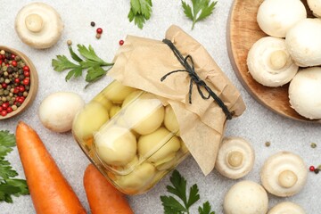 Tasty pickled mushrooms in jar and fresh ingredients on grey table, flat lay