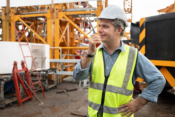 Caucasian mature engineer man worker use walkie talkie working with crane truck and spare crane background	