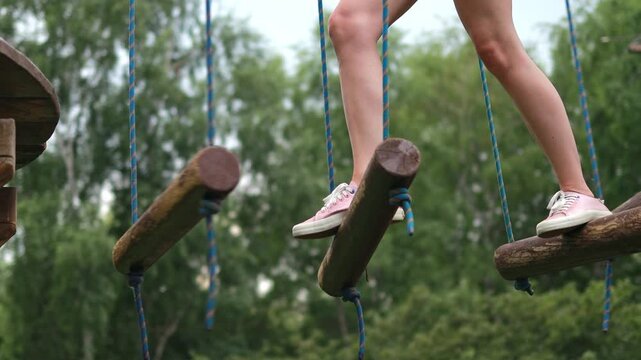 Close-up of a woman's legs running an obstacle course along parallel unstable bars in a rope park.