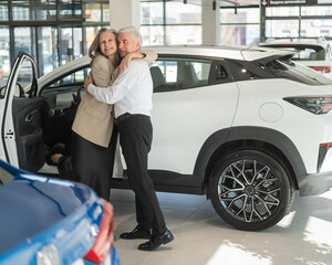 Mature Caucasian couple hugging with happiness while buying a new car. 