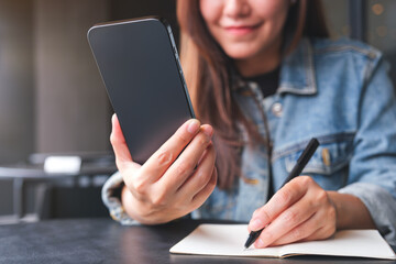 Closeup image of a woman writing on a notebook while using smart phone