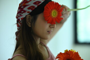 Brunette girl with a gerbera flowers. Face cover by flowers.