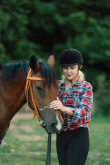 Obraz premium Happy blonde with horse in forest. Woman and a horse walking through the field during the day. Dressed in a plaid shirt and black leggings.