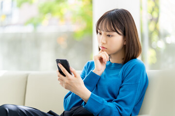 スマートフォンを見て考える若い日本人ビジネスウーマン