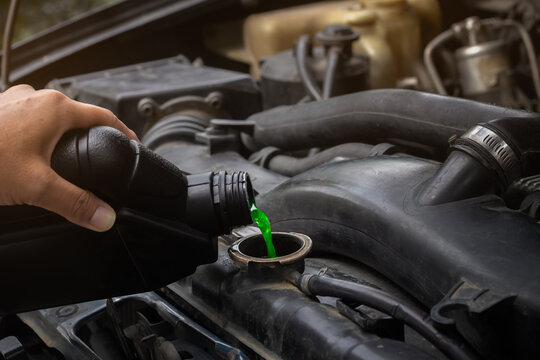 Mechanician hand filling pre-mixed green coolant into the radiator and car cooling system. Background for cars maintenance with selective focus and copy space.