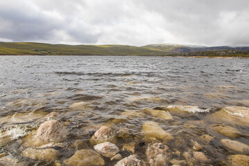 Shore of large transparent glacial lake with rocks on the surface. Embalse de Cenza. Vilariño de Conso Ourense