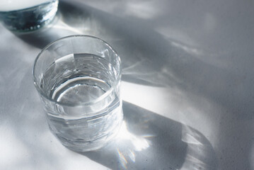 a glass of drinking water on white table in  morning sunlight.