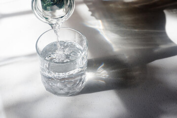 Pouring drinking water into glass on white table in morning sunlight.