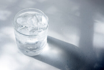 a glass of cold water with ice on white table in the morning sunlight.