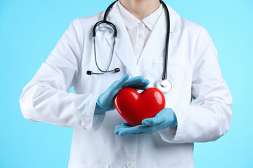 Doctor with red heart on light blue background, closeup