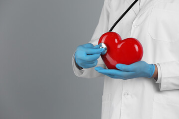 Doctor with stethoscope and red heart on grey background, closeup. Space for text