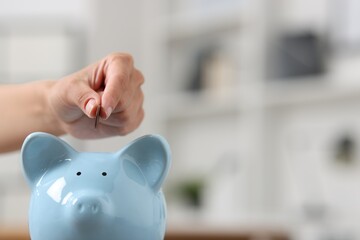 Woman putting coin into piggy bank against blurred background, closeup. Space for text