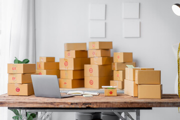 Parcel boxes on shelf and color shopping bags placing near laptop on table. SME business on shopping online at home office packaging on background is popular business.
